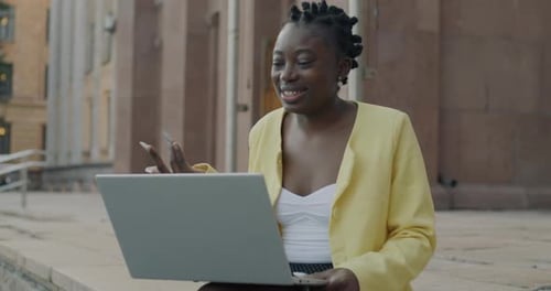 Joyful African American Girl Student Making Video Call with Laptop Talking Online Sitting in City