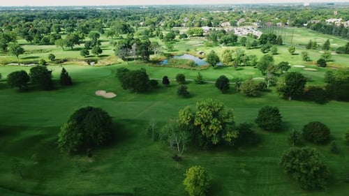 Aerial drone rotating shot over golf club covered with lush green grasslands along with small ponds