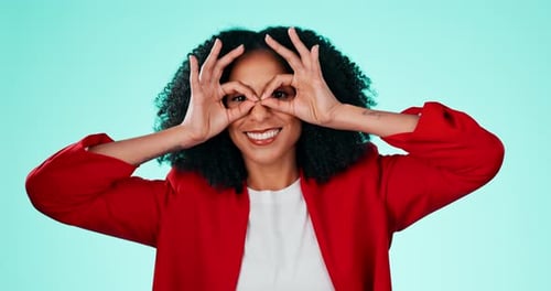 Face, fun and finger glasses with a black woman comic in studio on a blue background for humor