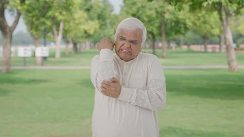 Sick Indian old man suffering from arthritis in park
