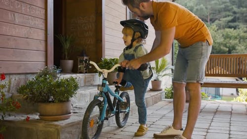 Father Helping Young Boy Ride Bike at Home