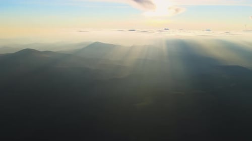 Aerial View of Dark Mountain Hills with Bright Sunrays of Setting Sun at Sunset Hazy Peaks and Misty