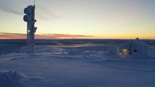 Reverse aerial view through snow covered cabin and tower on wintry Scandinavian hillside summit at s