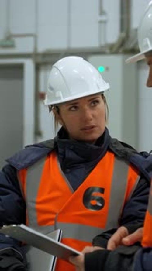Vertical of Man Shows Woman Inspection Plan on Clipboard in Storehouse