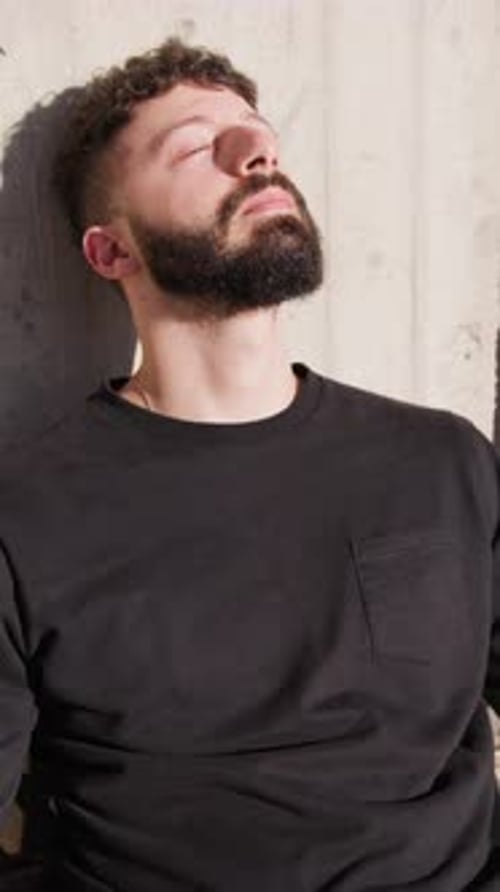 Bearded Man Resting Against Concrete Wall in Sunlight