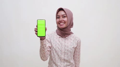 Young asian muslim girl standing while showing a blank cell phone screen. Isolated on white backgrou