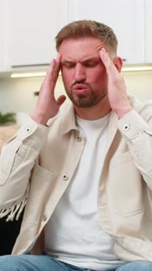 Man with headache rubbing his temples in home