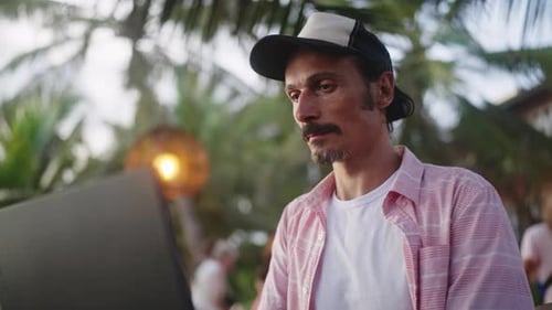 Freelancer arbeitet am Laptop bei Sonnenuntergang im Strandcafé Mann in Freizeitkleidung beschäftigt mit Remote-Job in der Nähe