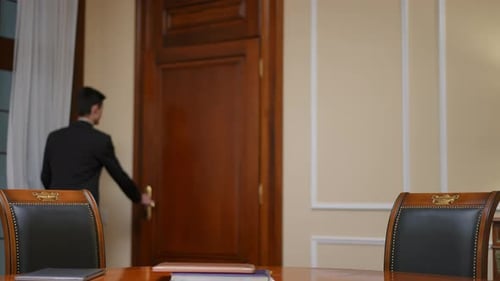 Man in Suit Enters Room, Leans on Table