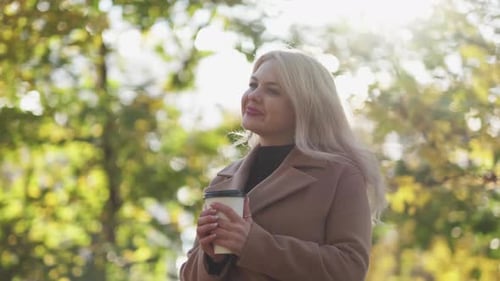 Woman Enjoying Coffee in a Sunny Autumn Park