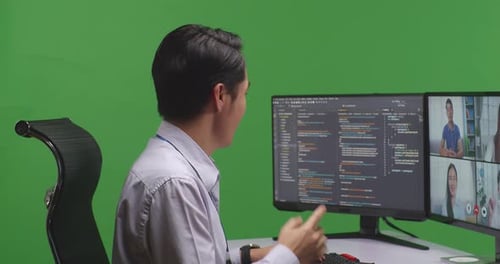 Nahaufnahme eines asiatischen Entwicklers, der Video hat, während er Code mit mehreren Bildschirmen auf grünem Bildschirm schreibt