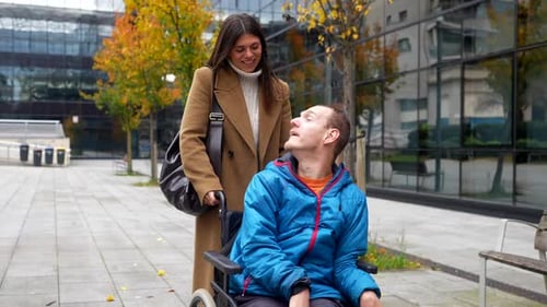 Caregiver pushing disabled man in wheelchair through a city park