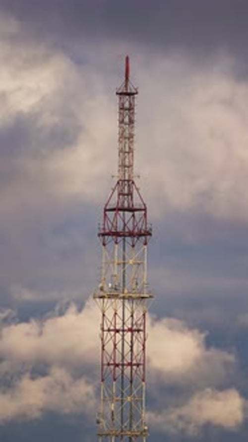 Timelapse na nuvem revela uma torre de telecomunicações em espiral branca e vermelha que se move em um ambiente dinâmico