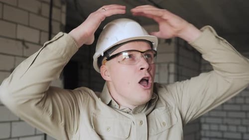 A Young Male Construction Worker in a Helmet Gets Scared and Grabs His Head