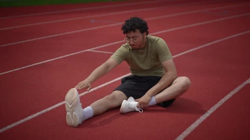Young Man Stretching Legs on Running Track