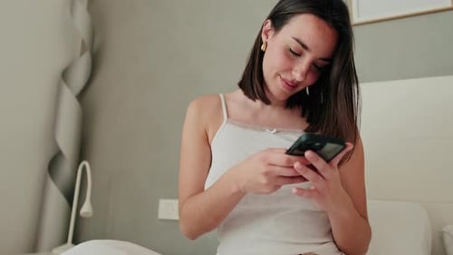 Woman Smiling Using Mobile Phone in Bedroom
