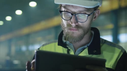 Engineer in hardhat is using a tablet computer in a heavy industry factory.