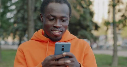 Smiling Young Man Using Mobile Phone in Park