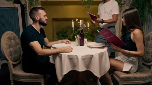 A young couple is sitting in an Italian restaurant the waiter gives the guests a menu of what order