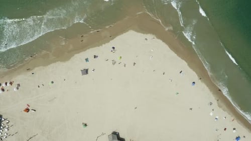 Aerial vertical top down view of calm ocean waves hitting the beach occupied with tourists enjoying