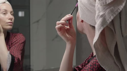 Woman Applying Eyebrow Makeup in Bathroom Mirror