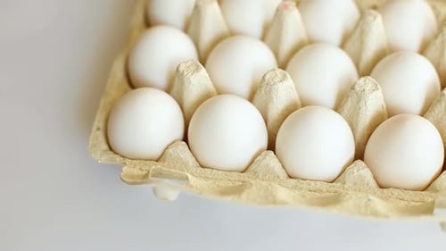 Rotation of cardboard box with white eggs on white background