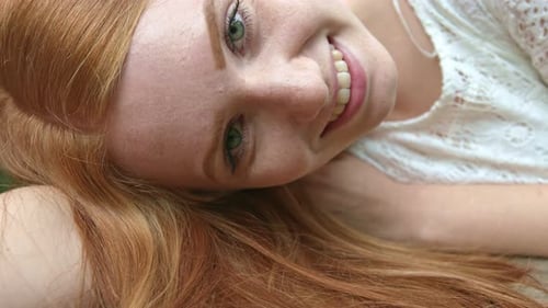Close up portrait of young ginger hair green eyes female lying on her side. Looking straight into ca