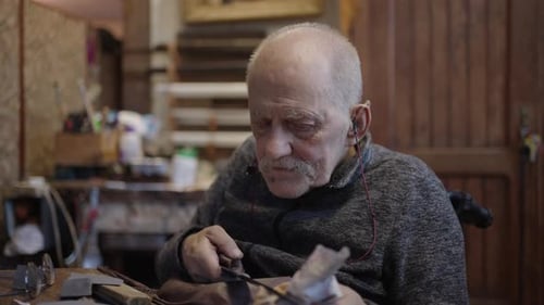 Senior Gray Haired Male Master in a Wheelchair Working at His Workshop Sharpening Japanese Swords