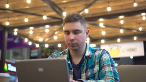 A Young Man is Sitting in a Cafe with a Laptop and Drinking a Hot Drink