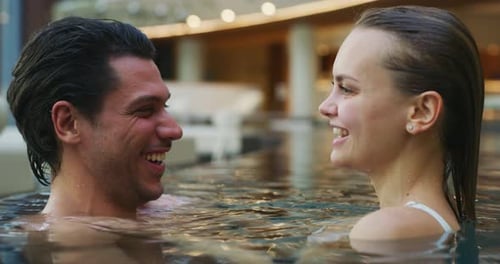 An young couple is embracing and having relax in an indoor illuminated with night lights swimming