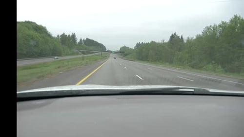 Driving under a large bridge spanning a river, divided freeway medium traffic, overcast day surround