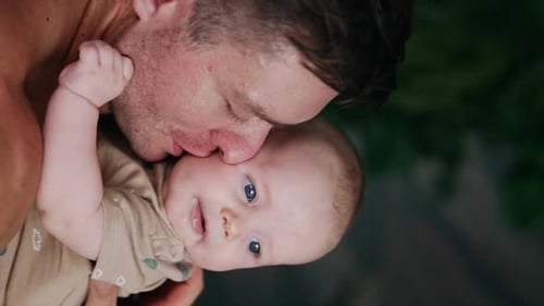 Unshaven Caucasian man kisses his little baby boy. Father and son portrait. Close up.