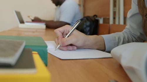 Hand Writing on Paper at Desk in Classroom