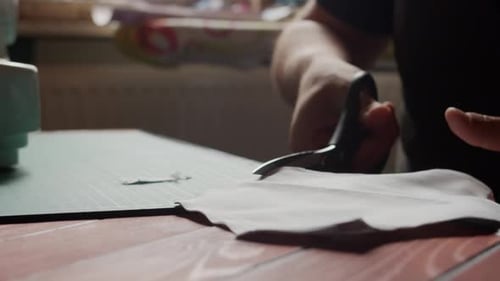 Découpe de tissu au ralenti avec des ciseaux sur une table rétroéclairée par la lumière naturelle.