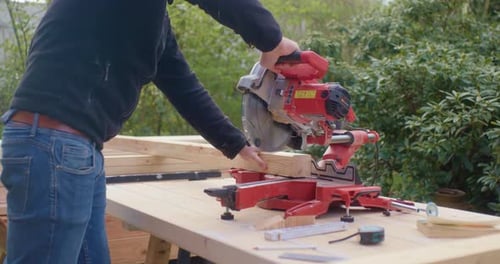 Man Cutting Wood With a Power Saw Outdoors