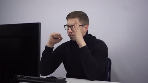An IT Specialist Works at a Computer and Looks Thoughtfully at a PC Monitor