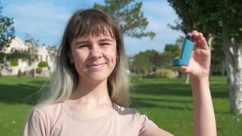 Smiling Girl Holding Asthma Inhaler in Park