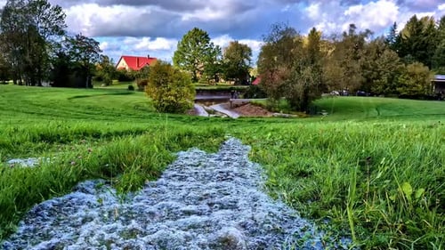 Freshwater River Rushing Through Grass Near Countryside Village. Static Shot