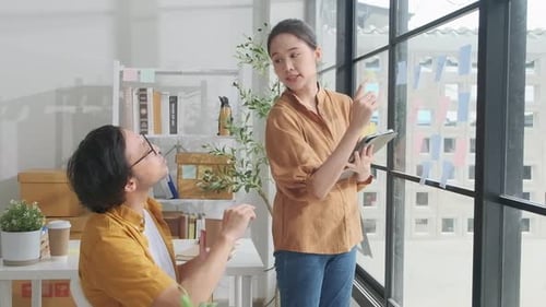 Two Asian startup partners are brainstorming at casual small business office.