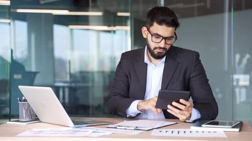 Busy businessman making financial calculations using calculator and laptop taking notes sitting