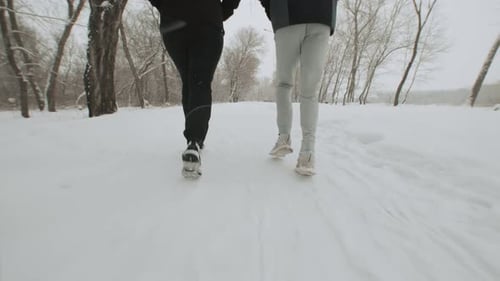 Two Athletes Running Next to Each Other Through a Snowy Road in a Winter Park in a Back View Two