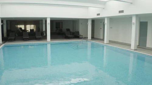 Drone Flying Over Clear Water Of Swimming Pool Towards Lounge Chairs In Hotel. - aerial