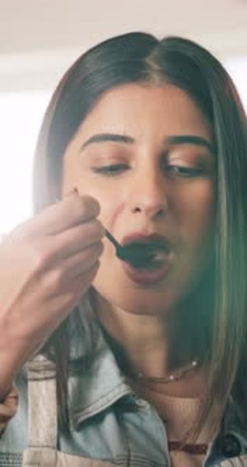 Woman Tastes Food with Spoon in Kitchen