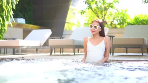 Attractive Chinese woman sitting in spa at luxury tropical island resort as water swirls in foregrou