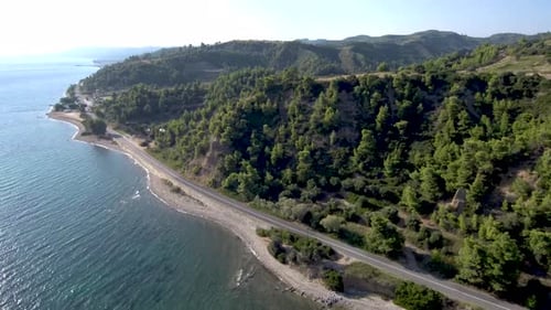 Aerial view of a road next to a beach and under a hilly hill in Greece