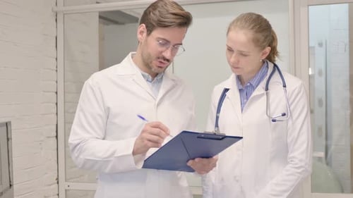 Doctors Collaborating over Clipboard in Medical Office