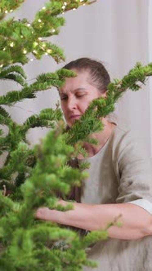 Woman Decorates Christmas Tree with Lights and Ornaments