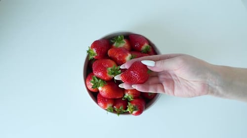 Woman's Hand Selecting Fresh Strawberries from Bowl