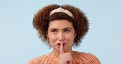 Whisper, face and woman with finger on lips in studio for secret, news or hush on blue background