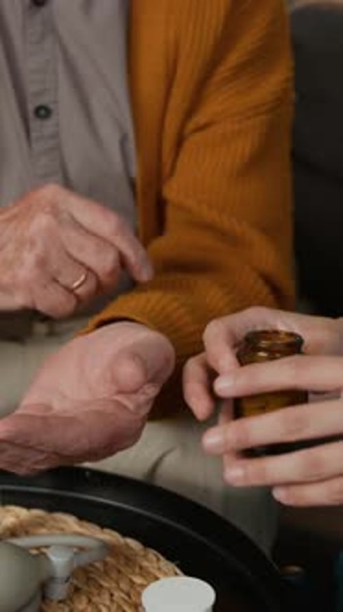 Senior Man Taking Pills from Young Woman's Hand